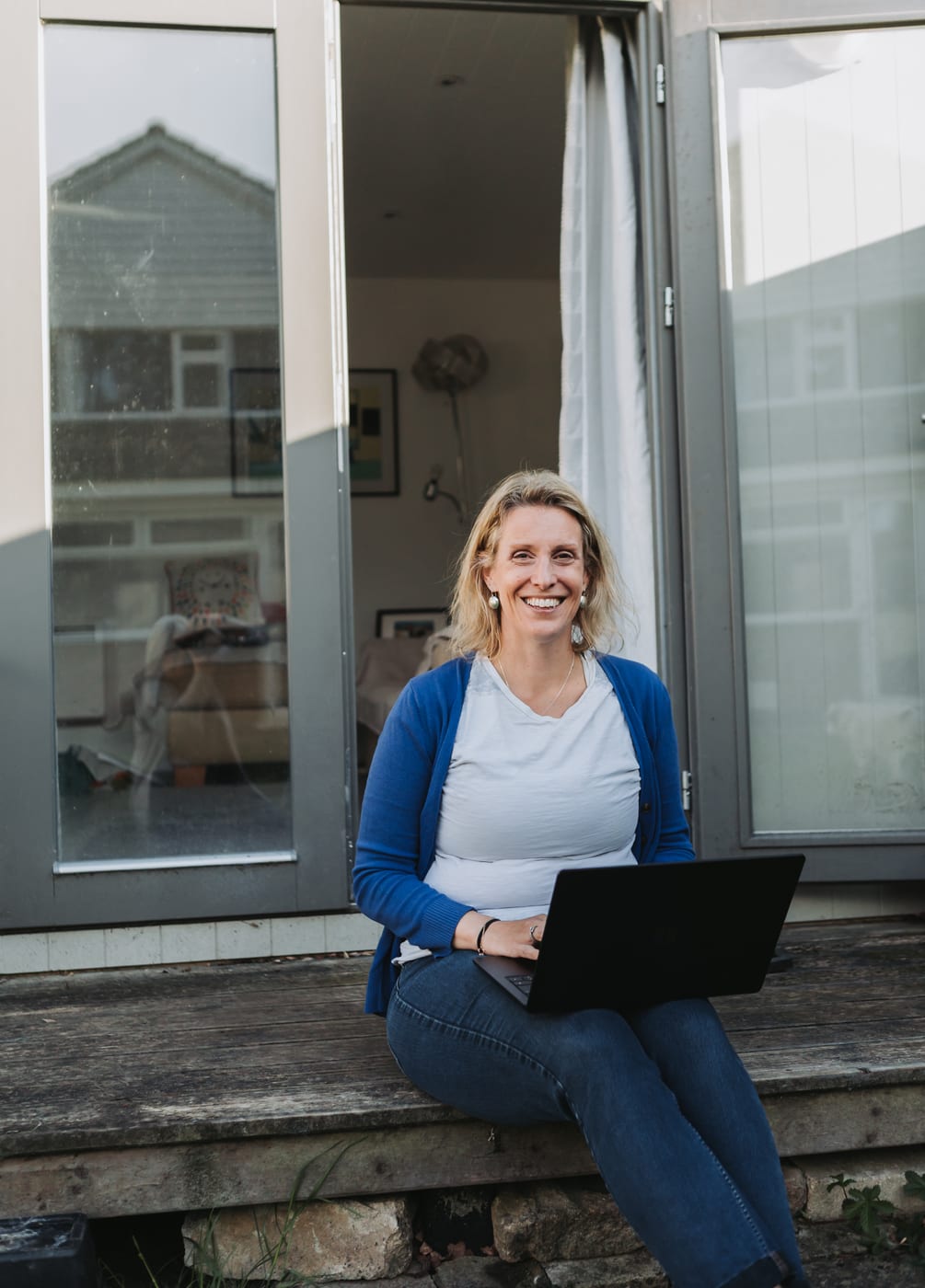 Dr Helen Ross working on her laptop on the step of her garden office